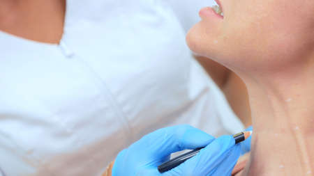 the beautician marks the injection points on the womans face with a pencilの写真素材