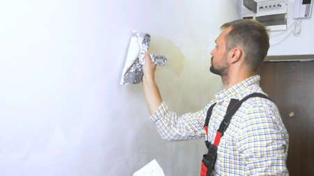 young handsome male builder lays plaster on the wall with a trowel. home repairsの写真素材