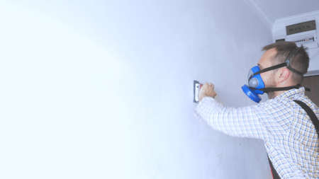 A worker in a respirator is grinding the wall with sandpaperの写真素材