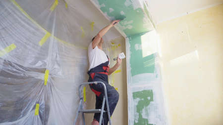 a man in overalls applies plaster with a spatula to the wallの写真素材