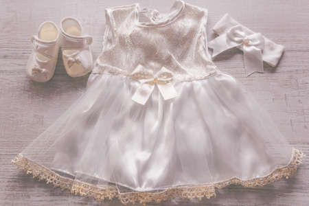 Christening baby dress, headband and shoes. Close-up of a cute newborn shoes, headband and a lace dress with a bow on a wooden background.の写真素材