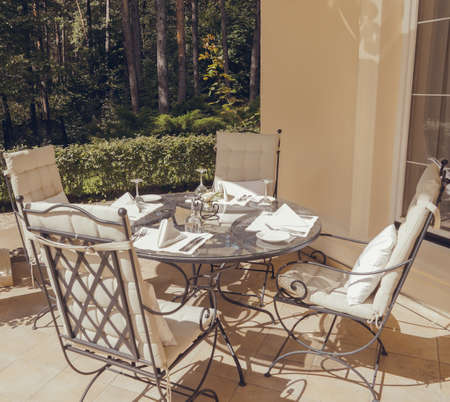 Beautiful summer terrace with garden furniture with white pillows surrounded by greenery on a warm, summer day.の写真素材