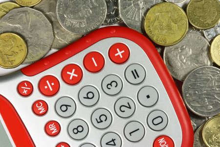 a red and silver calculator and coins scattered aboutの写真素材