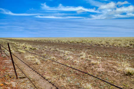 Australian outback with wire fence and dry grass and blue skyの写真素材