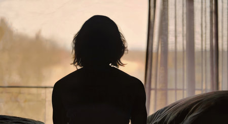 A powerful depiction of a woman in an abusive relationship, shown in a silhouette against window sitting on the edge of a bed, AI Generatedの写真素材