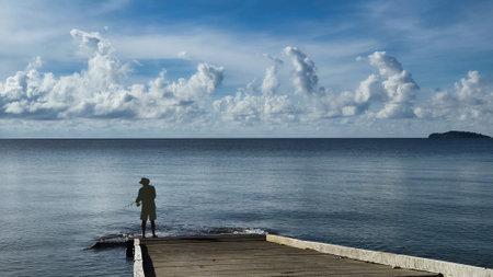 Cassowary Coast a peaceful seashore scene with a silhouette of a man fishing, distant islands dotting the horizon under a cloudy skyの写真素材