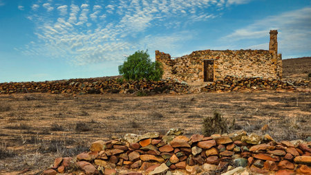 a striking old stone ruin under a textured sky, with earthy tones and strong leading lines from the rock walls. Old ruins in Kanyaka South Australiaの写真素材
