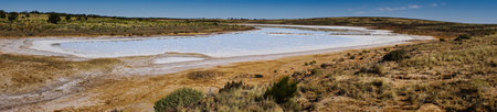National Hwy, Oakden Hills SA a vast desert salt lake stretches across a barren plain , a blue sky. Dry shrubs line the shore, with a salty shoreline and expansive horizon capturing rugged solitude.の写真素材