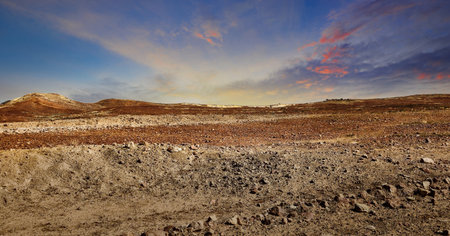 An expansive desert landscape featuring striking colors and textures with a cloudy sunset sky with hills in the horizon. On the road of the Oodnadatta Trackの写真素材