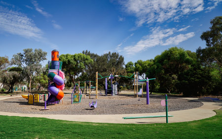 Bright playground in a sunny park features a tall spiral slide and colorful climbing structures, inviting outdoor fun, family time, and community play under a clear blue sky.の写真素材