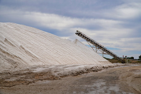 Large mounds of salt are stacked at a refinery in Thevenard. A conveyor system is used to transport the salt. The scene captures the scale and operations of this salt production facility. Eyre Peninsula in South Australiaの写真素材