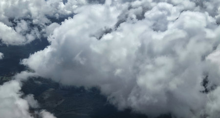 The scene shows clouds viewed from a plane flying above land. The clouds appear fluffy and white, with a blue background. This view captures the beauty of clouds in the sky.の写真素材