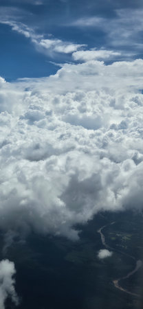 An expansive aerial scene showing dense white clouds beneath a blue sky, revealing a winding river and green countryside below.の写真素材