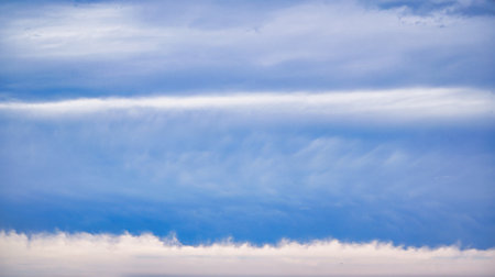 A tranquil blue sky filled with wispy white clouds stretches across the horizon, creating a peaceful, airy atmosphere.の写真素材