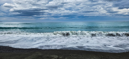 Moody coastal landscape featuring a pebbled shore, rolling waves, and a dramatic cloud-filled sky. New Zealandの写真素材