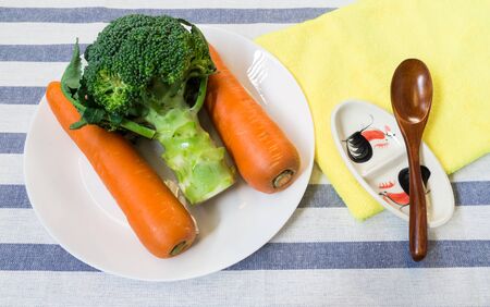Two Carrots and Broccoli on White Plate with Wooden Spoonの写真素材