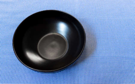 Empty Black Shine Ceramic Bowl on Blue Plain Backgroundの写真素材