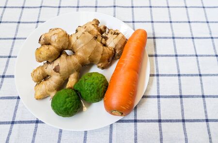Two Kaffir Limes with Galangal and Carrot on White Plate Placed on Squared Backgroundの写真素材