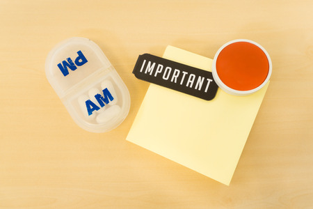 Reminder Pill Box with Important Word and Big Red Smile on Yellow paper Placed on Table Surfaceの写真素材