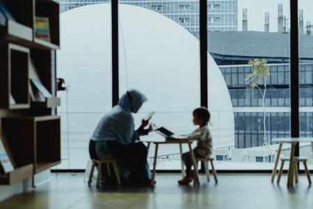 "Jakarta, Indonesia - October 2022: a mother is reading a book to her child at the Jakarta library, Taman Ismail Marzuki, she seems to be holding a cellphone in her right hand.のeditorial素材