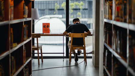 "Jakarta, Indonesia - October 2022: an asian man is sitting reading a book in a workspace in a jakarta library.のeditorial素材