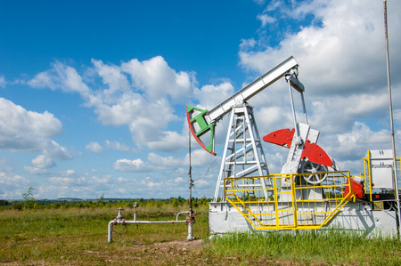 Oil and gas industry. Work of oil pump jack on a oil field. White clouds and blue sky. oil well pump. Oil and gas industry. Work of oil pump jack on a oil field.の写真素材