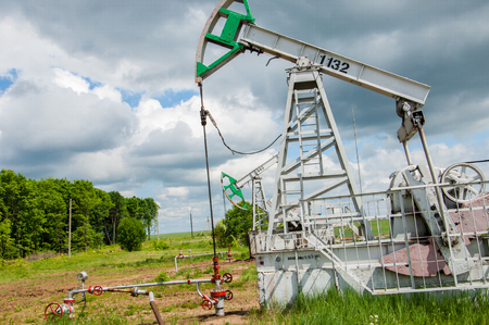 Oil and gas industry. Work of oil pump jack on a oil field. White clouds and blue sky. oil well pump. Oil and gas industry. Work of oil pump jack on a oil field.の写真素材