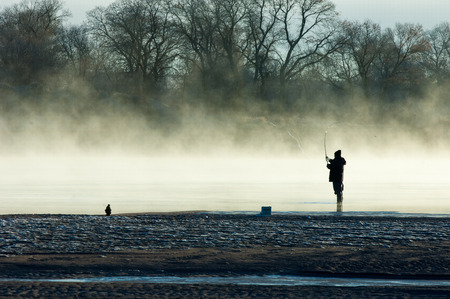 fishermen. A fisherman fight against a bass at sunset. Fisherman silhouette on the beach at colorful sunset. Fly fisherman walking beautiful landscapeの写真素材