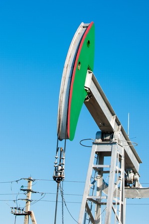 Oil rocking chair closeup. Oil rocking chair on a background of blue sky. The pumping unit as the oil pump installed on a well. Equipment of oil fields.の写真素材