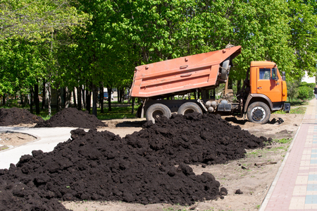 car dumper unloads the black earth on the flowerbed in city parkの写真素材