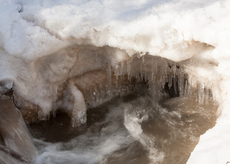 Streaming water in a small river at early springtime. Spring scene.  Mountain landscape with a frozen creekの写真素材