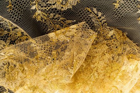 Image texture background, decorative gold lace with pattern. Golden vintage lacy background. Golden lace on a black background. Spandex, macro. Lacy decorative floral pattern.の写真素材