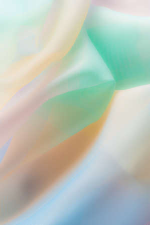 Blurry, not sharp sharpness. Texture, background, pattern. Silk fabric is transparent, yellow-pink green in blue. Abstract soft chiffon texture background.の写真素材