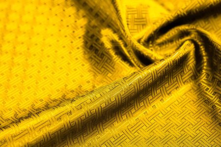 Background texture, pattern. Yellow, mustard silk fabric with a small checkered pattern. Muffled yellow braided with subtitles with sparkles - a bright chart-plot design. Individual pieces.の写真素材