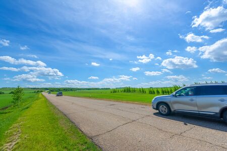 Spring photography, old asphalt road cracked by old age. It has a brown tint from the sun, wind and frost. crops grow along the edge of the road. Landscape charm calls for travelの写真素材
