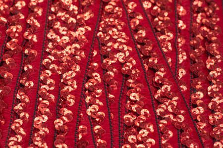 Red sequins. Ribbon for fabric decoration. Background texture, sunrise. Smooth slope of rows of round ruby sequins on a fine fabric mesh.の写真素材