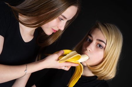 Girls and a banana. In black T-shirts and black shorts on a dark background.の写真素材