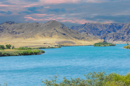 Enjoy the tranquil beauty of the sunset over the calm river. Immerse yourself in majestic mountains and lush green trees. Experience the peace and serenity of nature.の写真素材