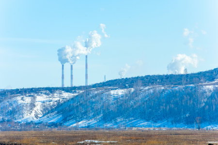 Spring remains of snow, in the background there are chimneys from the factory, in the foreground there is a treeの写真素材