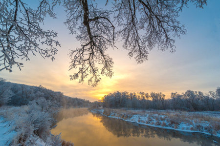 Experience the beauty of a winter wonderland at sunrise. The golden sun illuminates the enchanting frozen river. The whimsical and magical atmosphere creates a unique winter experience.の写真素材