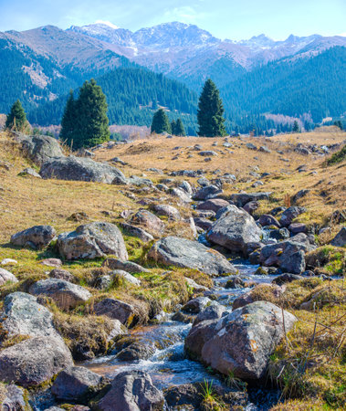 Immerse yourself in the tranquil beauty of nature. Enjoy the vibrant colors of fall and the soothing sound of the winding river. Experience the awesome Tian Shan Mountainsの写真素材