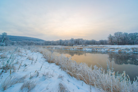 Winter Wonderland is a peaceful and serene place. The sun creates a beautiful golden light on the frozen river. The beauty of nature is showcased in this picturesque scene.の写真素材