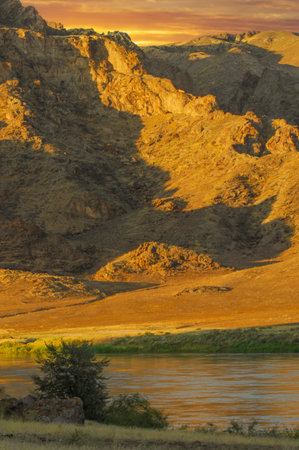 Witness the stunning contrast between jagged rocks, a flowing river and the golden hues of a mesmerizing sunset on the Natural Wonders steppeの写真素材