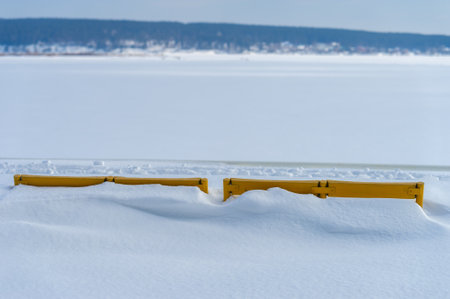 Capture the beauty of winter landscapes. Feel the brightness and warmth of a sunny day in the park. Focus on the contrast between the bright yellow bench and white snow. Highlight the serene atmosphere.の写真素材