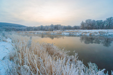 The frozen river is bathed in the warm golden light of the rising sun. A serene and tranquil winter...