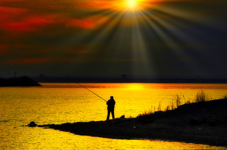 Golden moments: As the sun bids farewell to the day, a serene silhouette of a man engrossed in fishing captures the essence of tranquility at sunset. Sunset Fishing Golden Momentsの素材