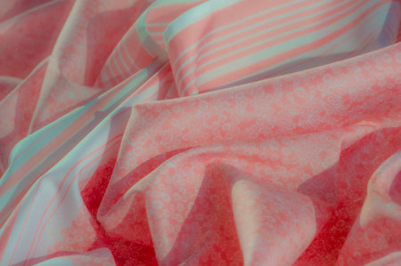 Soft fabric in coral tones with floral prints and pastel blue stripes, gently folded to reveal a...