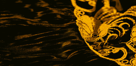 Textured fabric with embroidered golden patterns, revealing high contrast between light and shadows. The folds and embroidery create a dynamic visual flow and luxurious aesthetic.の写真素材