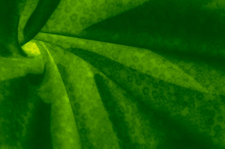 A glowing green fabric stretches in curved folds, with an intricate floral pattern adding depth. The light captures the vibrant, nature-inspired tones beautifully.の写真素材