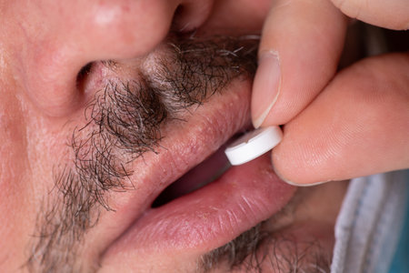 The young man is sick and lies in bed. He takes antipyretic pills to bring down his temperature.の写真素材